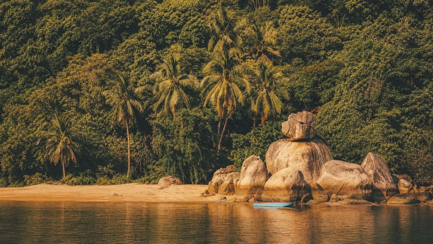 A quiet cove on the island: granite boulders, a small blue boat, jungle to the waterline